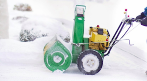 Gloved hands pushing a green and yellow snow blower.